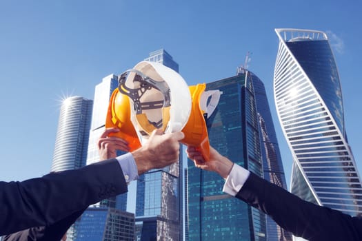 Group of business people clinking their helmets as a success on skyscrapers background, construction finished concept