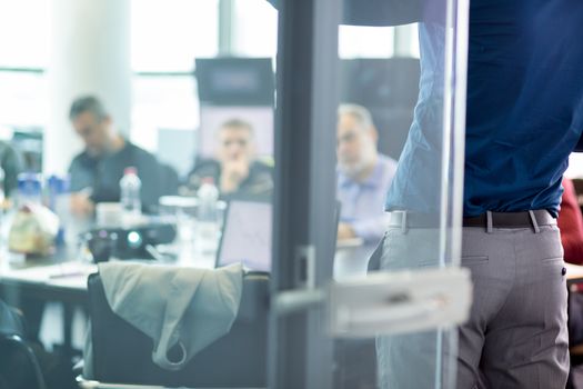 Business man making a presentation at office. Business executive delivering a presentation to his colleagues during meeting or in-house business training. View through glass.