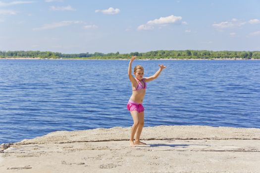 Dancing girl on the riverbank in pink swimsuit