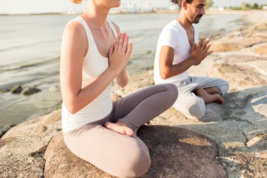 fitness, sport, people and lifestyle concept - close up of couple making yoga exercises sitting on pier outdoors