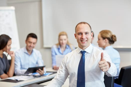 business, people, gesture and teamwork concept - smiling businessman showing thumbs up with group of businesspeople meeting in office