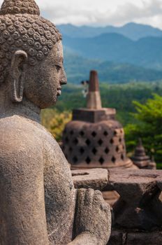 Sideview of a Buddha and a Stupa made of stone at Borobudur