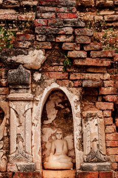 Sitting Buddha encarved in stone with bricks and plants surrounding him