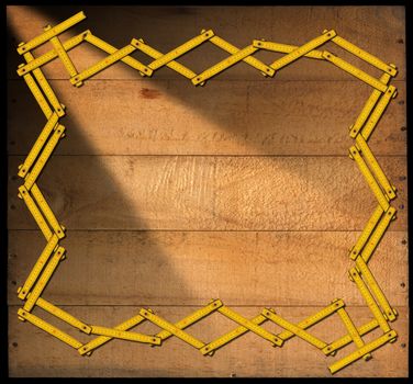 Border frame made from a old wooden ruler on a weathered wooden background with planks and nails. Isolated on black background