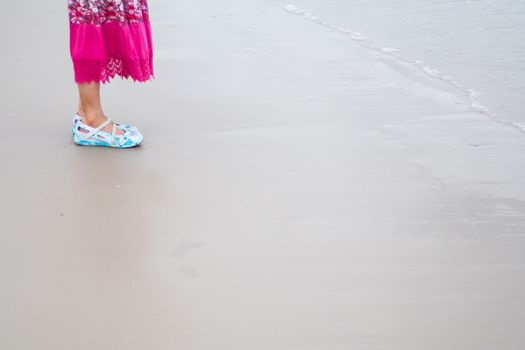 asian woman with pink long skirt and blue shoes standing by the sand beach