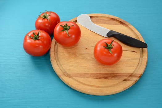 Four tomatoes on a round wooden chopping board with a tomato knife