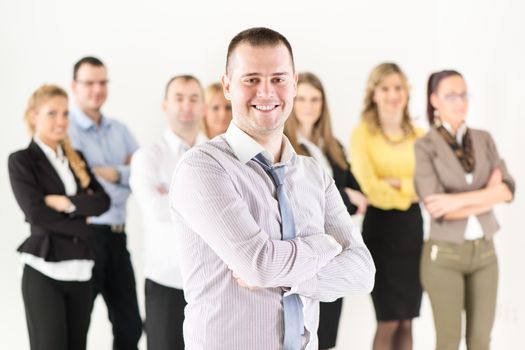 Successful and Smiling businessman with crossed arms standing in front of colleagues and looking at the camera.