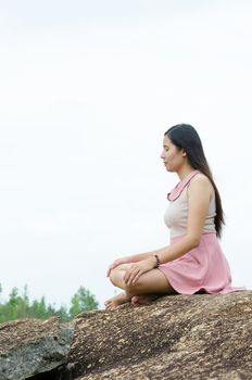 Woman Yoga meditation sitting on stones with mountains and white sky on background harmony with nature concept.