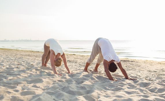 fitness, sport, friendship and lifestyle concept - couple making yoga exercises on sand outdoors