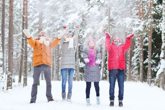 love, season, friendship and people concept - group of happy men and women having fun and playing with snow in winter forest