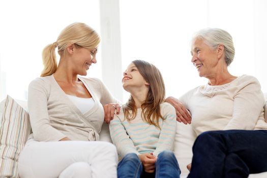 family, happiness, generation and people concept - smiling mother, daughter and grandmother sitting on couch at home