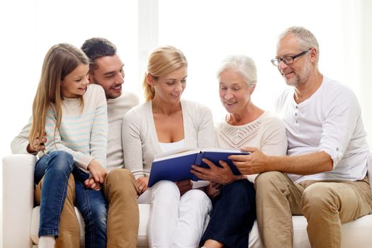 family, happiness, generation and people concept - happy family with book or photo album sitting on couch at home