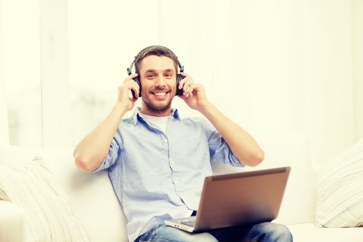 technology, home, music and lifestyle concept - smiling man with laptop and headphones at home