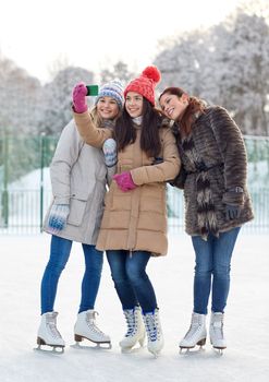 people, friendship, technology and leisure concept - happy girl friends taking selfie with smartphone on ice skating rink outdoors