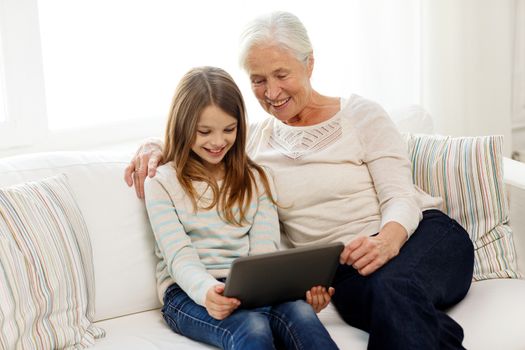 family, generation, technology and people concept - smiling granddaughter and grandmother with tablet pc computer sitting on couch at home