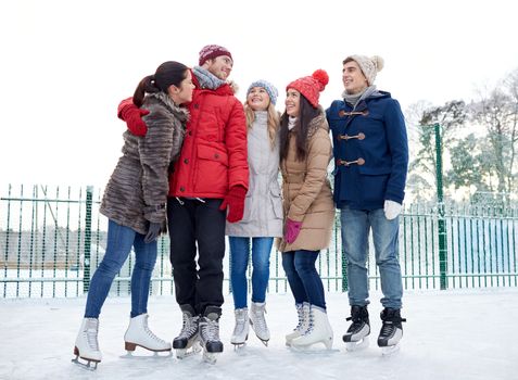 people, winter, friendship, sport and leisure concept - happy friends ice skating and hugging on rink outdoors