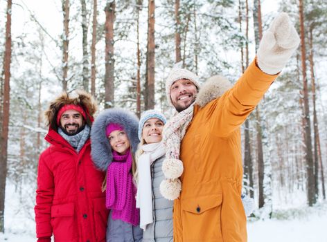 love, relationship, season, friendship and people concept - group of smiling men and women pointing finger in winter forest