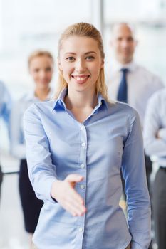 business, people and teamwork concept - smiling businesswoman making handshake gesture with group of businesspeople in office