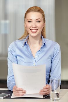 business and people concept - smiling woman holding papers in office
