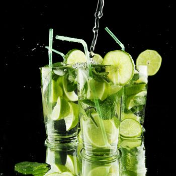 Pouring fresh mojito cocktail in glasses isolated on black background