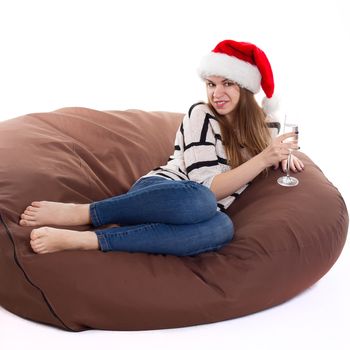 Cheerful girl in the Santa Claus hat. Girl sitting on a chair with a glass of champagne.