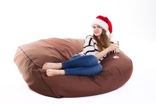 Cheerful girl in the Santa Claus hat. Girl sitting on a chair with a glass of champagne.