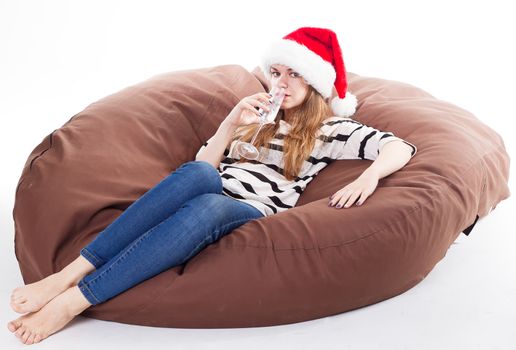 Cheerful girl in the Santa Claus hat. Girl sitting on a chair with a glass of champagne.