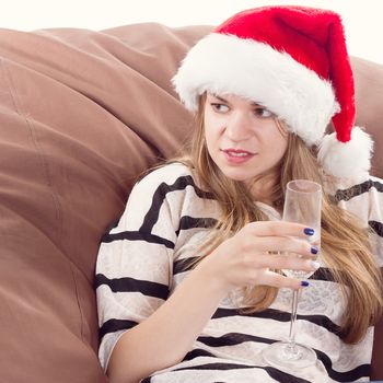 Cheerful girl in the Santa Claus hat. Girl sitting on a chair with a glass of champagne.