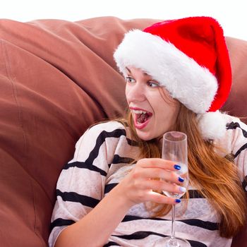 Cheerful girl in the Santa Claus hat. Girl sitting on a chair with a glass of champagne.