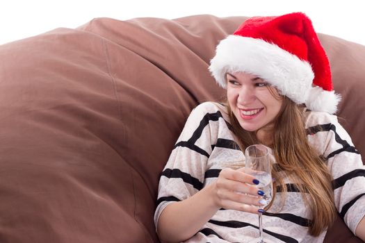 Cheerful girl in the Santa Claus hat. Girl sitting on a chair with a glass of champagne.