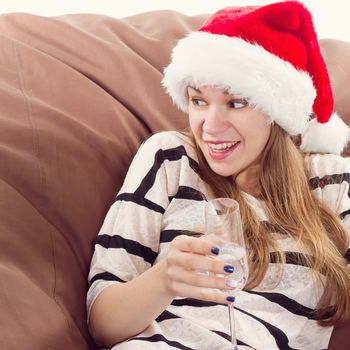 Cheerful girl in the Santa Claus hat. Girl sitting on a chair with a glass of champagne.