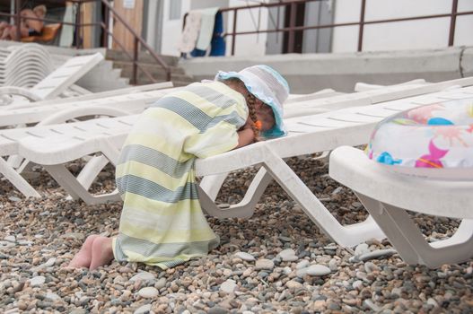 The three-year girl capricious and roars leaning on a chaise longue at the seaside