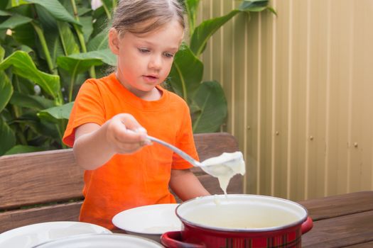 Four-year girl on breakfast imposes a ladle into a bowl semolina