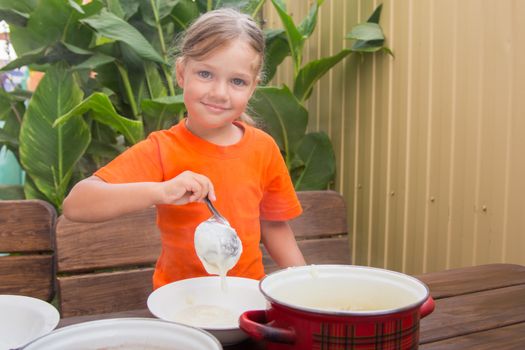 Four-year girl on breakfast imposes a ladle into a bowl semolina