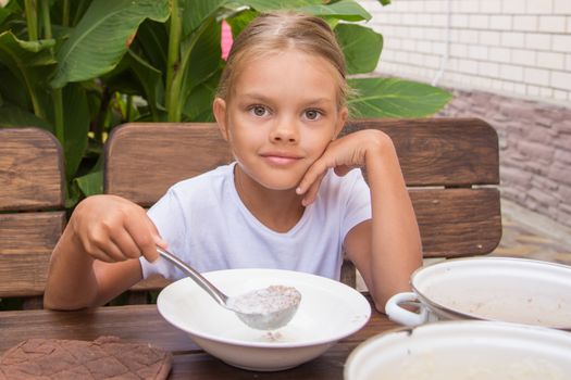 Six year old girl at breakfast imposes a ladle into a bowl buckwheat