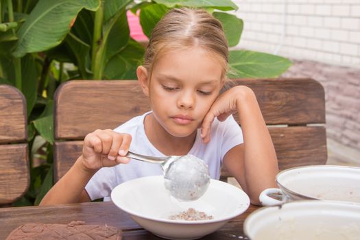 Six year old girl at breakfast imposes a ladle into a bowl buckwheat