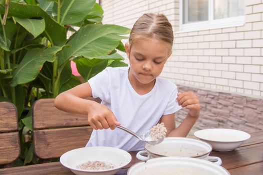Six year old girl at breakfast imposes a ladle into a bowl buckwheat