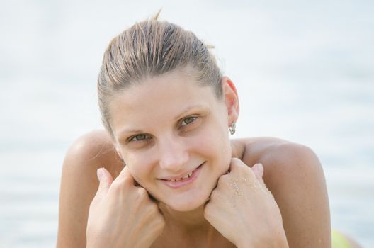 Twenty-five year girl lies on her stomach on the sand by the river