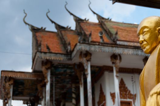 Golden Buddha with beautiful ancient temple in Laos under a cloudy but blue sky