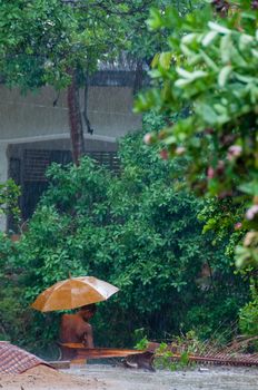 Orange monk with umbrella in the rain in Cambodia