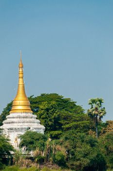 Gold white Pagoda Stupa at Irrawaddy river between trees und a blue sky on the way to Mandalay