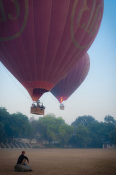 Asian Man sitting in front of two hot air balloons Bagan Myanmar Burma