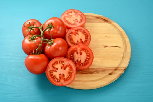 Red vine tomatoes whole and halved on a circular wooden board with copy space