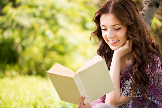 Beautiful Girl reading book in the park, sitting on the grass and Expressing Positivity.