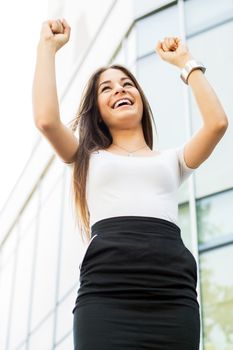 Successful Businesswoman standing on the street in front of Office Building with Arms Raised.