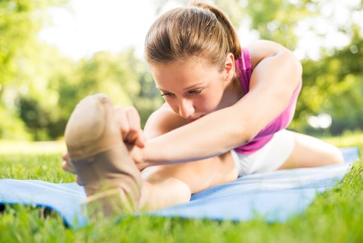 Cute young woman doing stretching exercises in the park. Close Up.