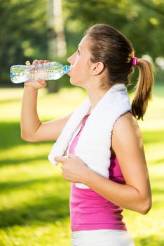 Beautiful young woman resting and drinking water after exercising in the park.
