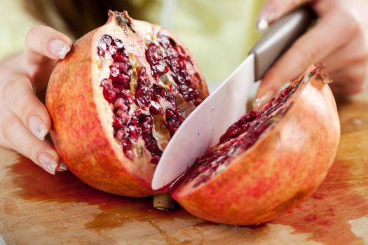 Female hands Cutting pomegranate in a kitchen. Close-up. Selective Focus.