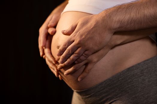 Two pairs of hands on pregnant woman's belly .