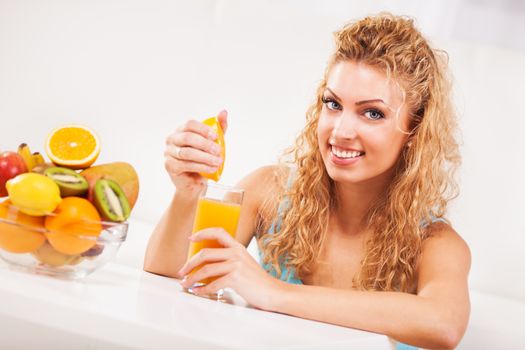 Beautiful young woman squeezes orange juice in the glass